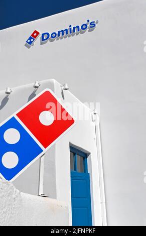 Mykonos, Grèce - 2022 juin : panneau situé à l'extérieur d'un comptoir à pizza Domino's. Le bâtiment est couvert de blanc traditionnel. Banque D'Images