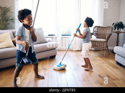 Deux petits garçons de course mixte jouant avec un balai et un balai dans le salon à la maison. Joyeux frères et sœurs s'amusant à jouer avec des fournitures de nettoyage à la maison Banque D'Images