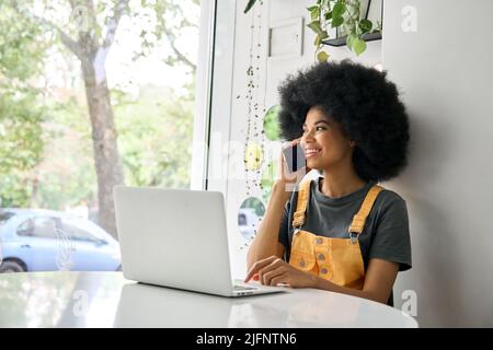 Jeune femme heureuse parlant au téléphone en utilisant un ordinateur portable dans un café. Banque D'Images