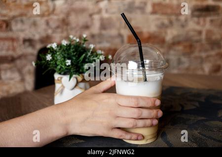 Un gros plan de la main d'une jeune femme prend une tasse de café froid d'une table dans un café. Boissons froides. Mise au point sélective. Banque D'Images