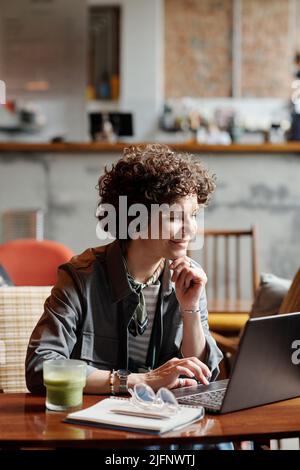 Bonne femme d'affaires d'âge moyen ou pigiste assis à table dans le café devant l'ordinateur portable et la mise en réseau ou la communication dans le chat vidéo Banque D'Images