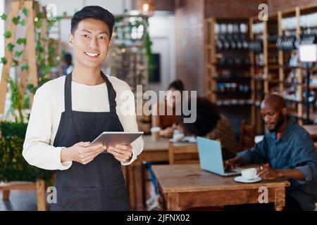 Portrait d'un propriétaire de petite entreprise asiatique souriant dans son restaurant muni d'une tablette numérique sans fil. Un jeune homme d'affaires qui utilise une tablette numérique Banque D'Images