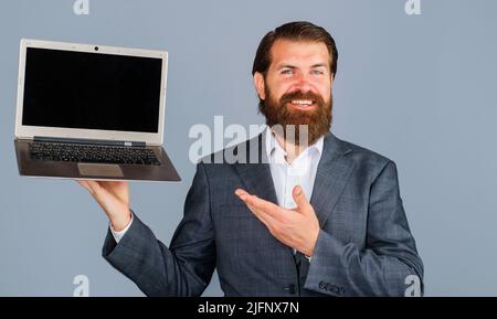 Un homme d'affaires souriant se présente avec la main sur un ordinateur portable. Homme barbu avec ordinateur. Écran vide sur l'ordinateur portable. Banque D'Images