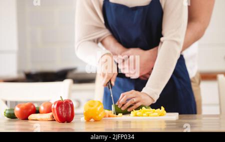 Cuisiner avec amour. Photo d'un homme qui embrasse sa femme pendant qu'elle prépare un repas dans la cuisine. Banque D'Images