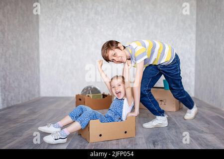 Frère manne sœur dans une boîte en carton. Les enfants jouent avec des boîtes à la maison en quarantaine. Un garçon et une fille ont déménagé dans un nouvel appartement et sont Banque D'Images