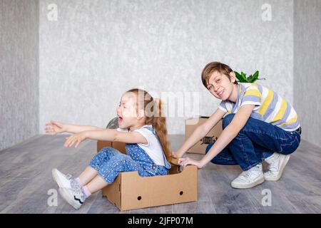 Frère manne sœur dans une boîte en carton. Les enfants jouent avec des boîtes à la maison en quarantaine. Un garçon et une fille ont déménagé dans un nouvel appartement et sont Banque D'Images