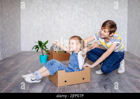 Frère manne sœur dans une boîte en carton. Les enfants jouent avec des boîtes à la maison en quarantaine. Un garçon et une fille ont déménagé dans un nouvel appartement et sont Banque D'Images