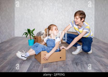 Frère manne sœur dans une boîte en carton. Les enfants jouent avec des boîtes à la maison en quarantaine. Un garçon et une fille ont déménagé dans un nouvel appartement et sont Banque D'Images