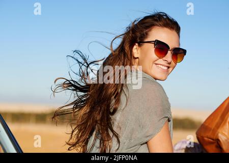 Il est aussi réel qu'il se trouve sur la route. Portrait d'une jeune femme attrayante souriant portant des lunettes de soleil à pavillon. Banque D'Images