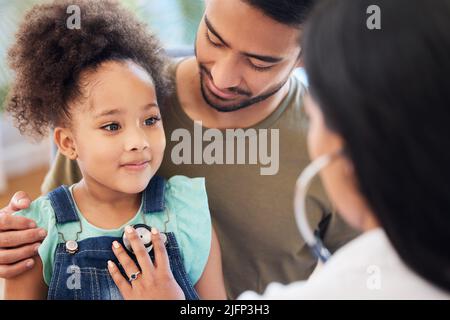 Mon médecin est vraiment gentil. Prise de vue d'une petite fille assise sur les genoux de son père tout en étant examinée par son médecin. Banque D'Images