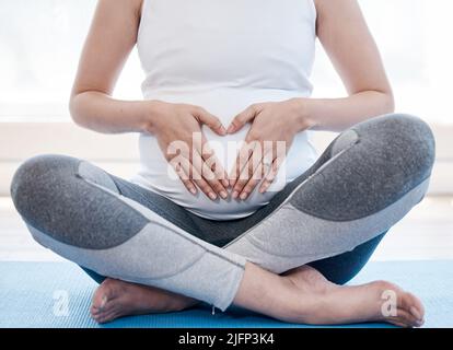 Voici mon cœur. Photo d'une femme enceinte faisant du yoga à la maison. Banque D'Images
