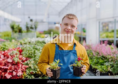 Jeune employé heureux avec le syndrome de Down travaillant dans le centre de jardin, prenant soin des fleurs. Banque D'Images