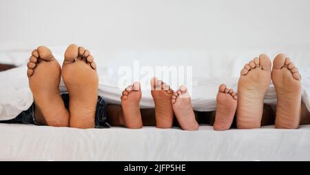 C'est trop confortable pour se lever. Photo d'une famille qui s'est posée pieds nus sur un lit à la maison. Banque D'Images