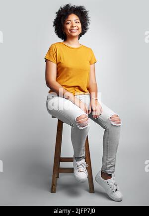 Partagez votre histoire. Photo studio d'une belle jeune femme assise sur une chaise sur fond gris. Banque D'Images