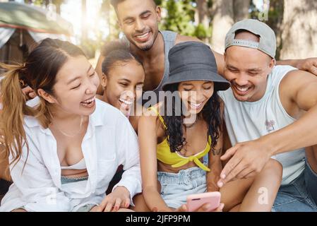 Shes le plus drôle du groupe. Photo d'un groupe diversifié d'amis se liant ensemble et en utilisant un téléphone cellulaire dans les bois. Banque D'Images