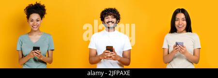 Photo panoramique de trois personnes multiraciales, de type indien, de femmes afro-américaines et chinoises, en utilisant des smartphones, en tapant des sms, en discutant, en regardant l'appareil photo, souriez, debout sur un fond orange isolé Banque D'Images