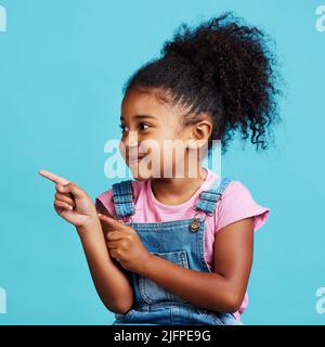 Je dis à tout le monde. Photo d'une adorable petite fille montrant quelque chose en se tenant sur un fond bleu. Banque D'Images