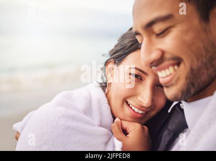 Je promets d'être un confort de réchauffement dans le froid. Photo d'un jeune couple sur la plage le jour de leur mariage. Banque D'Images