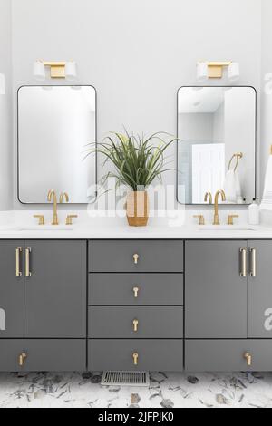 Salle de bains avec meuble-lavabo gris, lampes et robinets dorés et comptoir en marbre blanc. Banque D'Images