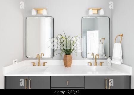 Salle de bains avec meuble-lavabo gris, lampes et robinets dorés et comptoir en marbre blanc. Banque D'Images