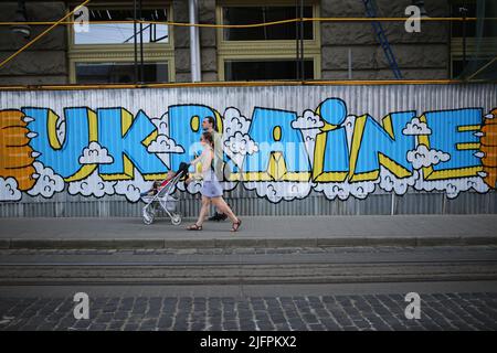 Lviv, Ukraine. 30th juin 2022. Une famille avec un enfant dans une poussette passe devant un mur avec des graffitis Ukraine. Graffiti pour soutenir l'Ukraine et Azov. Crédit : SOPA Images Limited/Alamy Live News Banque D'Images