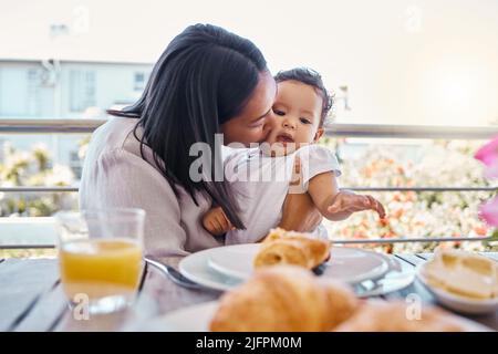 Il y a tellement de choses à apprécier. Photo d'une jeune mère embrassant son bébé tout en déjeunant à la maison. Banque D'Images