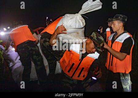 BEIHAI, CHINE - le 4 JUILLET 2022 - des policiers et des soldats armés utilisent des sacs de sable, des piquets et des planches de bois pour construire un barrage pour bloquer la brèche à Beihai Banque D'Images