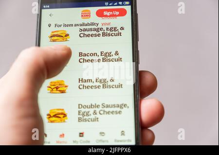 L'homme commande de la nourriture sur son téléphone. La main d'un homme choisit un hamburger au menu. Burger King Corporation est une société américaine qui possède une chaîne mondiale de foo rapide Banque D'Images