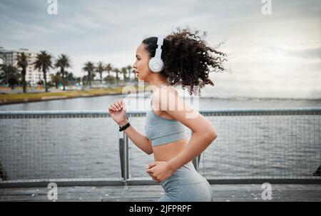 Shes off. Prise de vue courte d'une jeune athlète féminine attirante écoutant de la musique pendant sa course matinale à l'extérieur. Banque D'Images