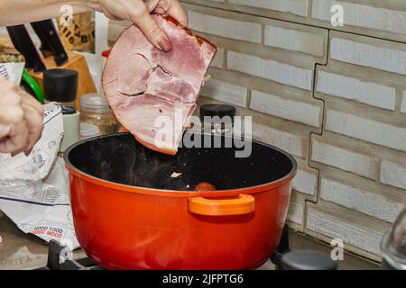 Le chef met un morceau de porc fumé dans le pot pour faire de la choucroute alsacienne Banque D'Images
