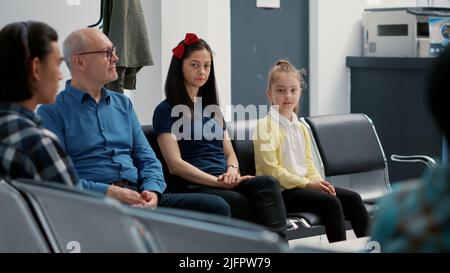 Portrait de la jeune mère et de la petite fille assis dans la salle d'attente, ayant rendez-vous avec un médecin à la clinique médicale. Femme avec enfant dans le hall de réception de l'hôpital, attendant dans la rangée. Banque D'Images