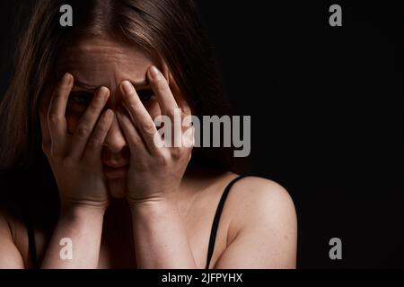 C'est à nouveau ce qui se passe. Photo d'une femme qui a l'air effrayée en se tenant debout contre un arrière-plan sombre. Banque D'Images