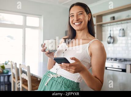 Bien commencer la journée. Photo d'une femme tenant son téléphone portable tout en buvant du café à la maison. Banque D'Images