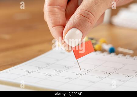 Les mains corrigeant l'horaire des notes, la vignette du drapeau rouge dans le calendrier pour la réunion et le rappel de rendez-vous Banque D'Images