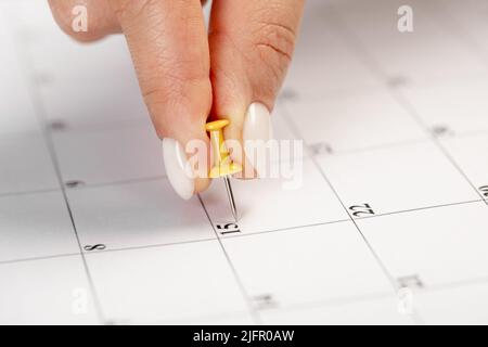 une main féminine avec une belle manucure tient une punaise jaune pour marquer la date sur le calendrier Banque D'Images