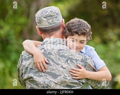 Une famille est un groupe de personnes qui aiment inconditionnellement. Coup de feu d'un père revenant de l'armée embrassant son fils à l'extérieur. Banque D'Images