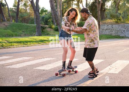 Jeune homme frais tatoué enseignant à sa girafe comment faire du skateboard. Banque D'Images