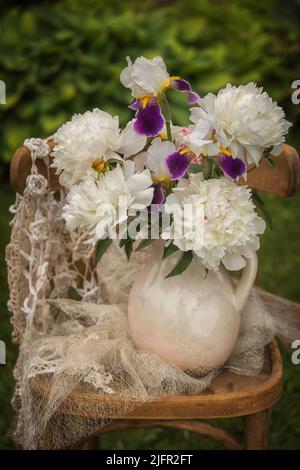 Bouquet d'iris barbu et de pivoines blanches sur une chaise. Banque D'Images