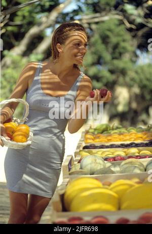 jolie auburn cheveux jeune femme achetant des fruits sur fond de feuillage vert du marché silhouette attrayante Banque D'Images