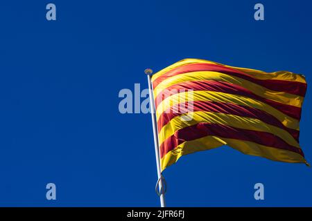 Le drapeau de la Catalogne (Espagne) flotte dans le vent. Sur le côté gauche de l'image se trouve une grande zone d'espace négatif créée par le ciel bleu. Banque D'Images