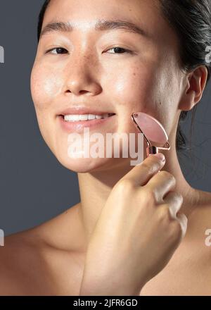 Ma peau vous dit si cela fonctionne ou non. Photo studio d'une belle jeune femme utilisant un rouleau de visage sur sa peau. Banque D'Images