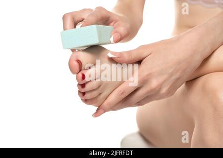 femme limer ses pieds avec une pierre ponce sur fond blanc studio. Banque D'Images