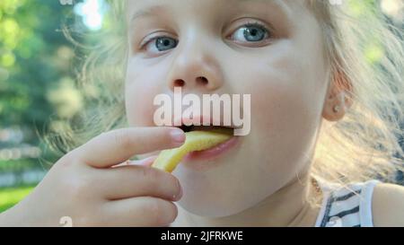 Odessa, Ukraine, Europe de l'est. 4th juillet 2022. Une petite fille mange des frites. Gros plan de blonde fille prend des chips de pomme de terre avec ses mains et les essaie assis dans la rue café sur le parc. (Credit image: © Andrey Nekrasov/ZUMA Press Wire) Banque D'Images