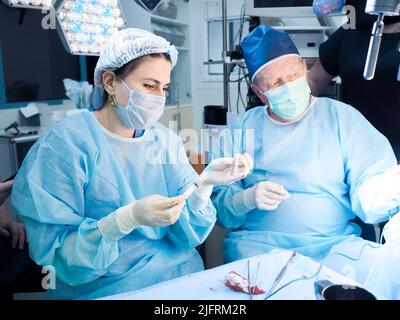 Moscou. Russie. 24 décembre 2021. Jeune femme chirurgien avec une seringue pendant la chirurgie. Mise au point sélective. Professionnel confiant. Une femme médecin assiste un chirurgien expérimenté âgé en chirurgie. Banque D'Images