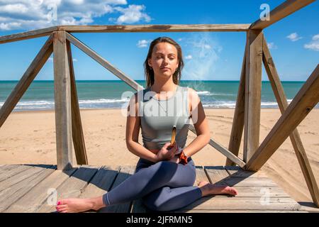 femme méditant par la plage avec un bâton de palo santo Banque D'Images