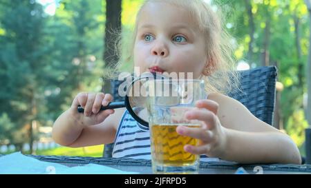 Odessa, Ukraine, Europe de l'est. 4th juillet 2022. La petite fille regarde dans l'objectif autour. Gros plan d'une fille blonde étudiant le monde autour d'elle la regardant à travers la loupe tout en étant assise dans un café de rue sur le parc. (Credit image: © Andrey Nekrasov/ZUMA Press Wire) Banque D'Images