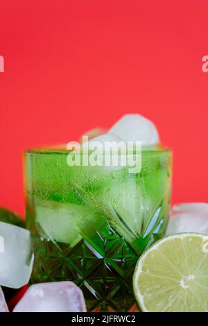 gros plan des glaçons surgelés en verre avec mojito vert étincelant et limes sur le rouge Banque D'Images