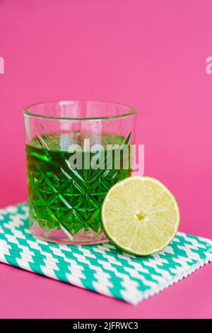 verre d'alcool vert sur pailles en papier à rayures près de la chaux sure sur rose Banque D'Images