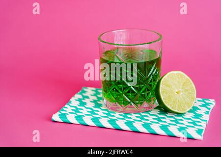 verre d'alcool vert sur pailles en papier à rayures près de lime tranché sur rose Banque D'Images