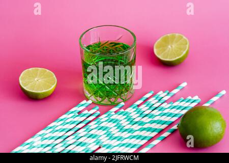 verre d'alcool vert boire près de pailles en papier à rayures sur rose Banque D'Images